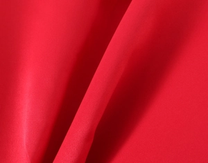 Detailed close-up of premium red woven fabric with silky texture and soft draping