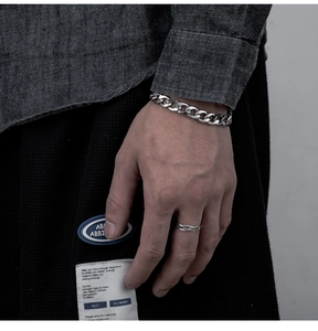 Close-up of a silver Cuban link bracelet and twisted rope ring on a male model wearing denim