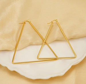 Detailed view of polished large golden triangle hoop earrings on champagne silk fabric