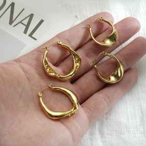 Macro detail of hand-held bright gold earrings with modern irregular twisted metal texture