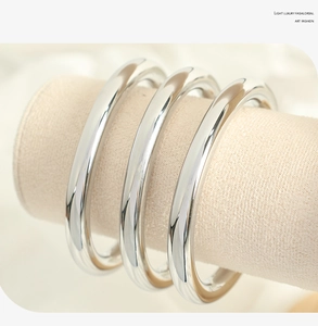 Close-up of three wide silver titanium steel bangles on a minimalist display stand