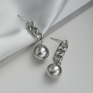 Close-up of high-polished silver chain earrings with metal sphere pendant on silk fabric