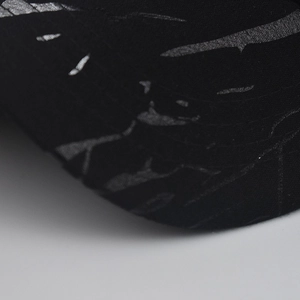 Macro shot of silver cracked print on black baseball cap fabric showing stitching detail