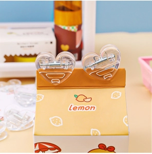 Close-up of a heart-shaped transparent acrylic clip with a strong metal spring on a box