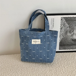Detail of blue denim tote bag with white embroidered bows and hearts on soft rug