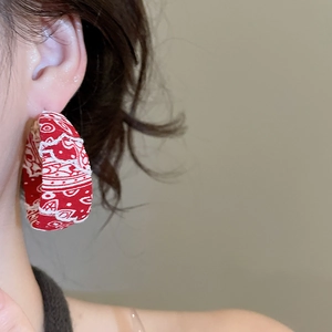 Gros plan de créoles en tissu à motif paisley rouge portées par un mannequin