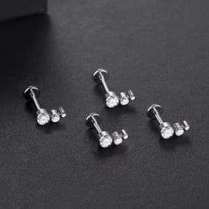 Detailed view of silver titanium labret studs with three clear crystals on black background
