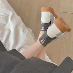 Close-up of dark grey cotton socks with pink bow embroidery worn with chunky sneakers