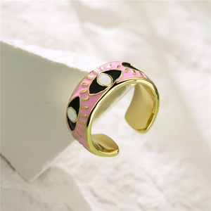 Macro detail of gold-plated pink enamel evil eye ring on a white textured stone base