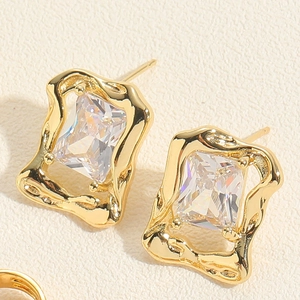 Detail of rectangular 14K gold plated earrings with zircon stone on textured background