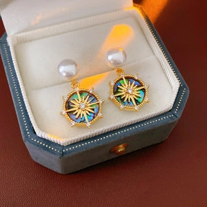 Detail of gold-plated mother of pearl star earrings resting in a blue jewelry box
