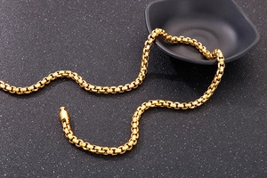 Detail of gold box chain necklace with cylindrical clasp on black textured background