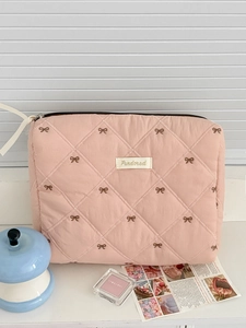 Close-up of pink quilted cosmetic bag with brown bow embroidery and branded fabric label
