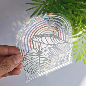 Close-up of rainbow prism suncatcher sticker with monstera leaf on a glass surface