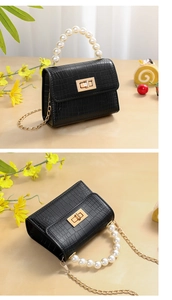 Detail of black crocodile texture mini bag with pearl handle and gold twist lock