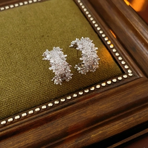 Macro shot of silver C-shaped earrings with micro-paved zircons on green fabric