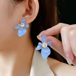 Gros plan de boucles d'oreilles fleurs en résine bleue avec zircon portées par un modèle