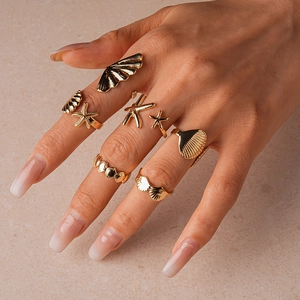 Detail of 7-piece gold starfish and seashell rings on a hand for beach vacation style
