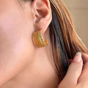 Close-up of gold C-shaped hoop earrings with hammered texture and zircon inlays on model