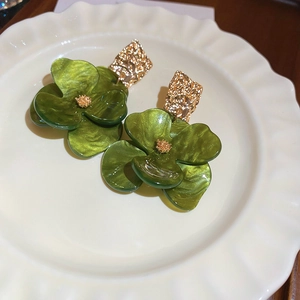 Macro detail of green acrylic flower earrings with golden hammered metal texture