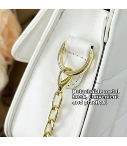 Macro detail of the golden lobster clasp and D-ring on the white leather shoulder bag