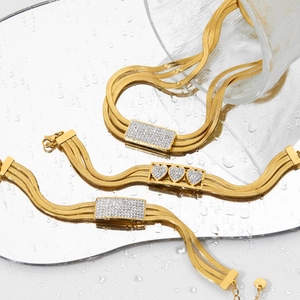 Golden multi-layer herringbone bracelet set with sparkling heart zircon on a mirror surface
