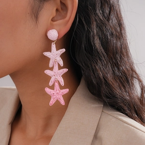 Close-up of model wearing pink woven raffia starfish fringe earrings for summer