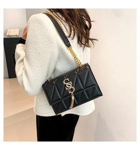 Detail of black quilted shoulder bag featuring gold chain strap and S-logo tassel