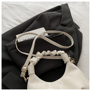 Detail der weißen Hobo-Tasche mit Marmor-Textur und gerafftem Griff auf Blazer
