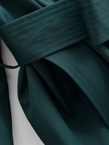 Detailed macro view of dark green trench coat with thick twill fabric and waist belt