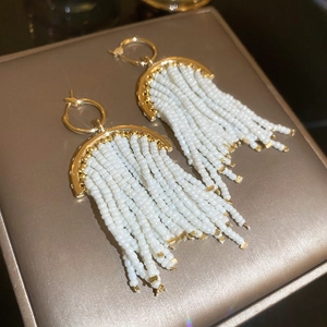 Détail des boucles d'oreilles dorées à franges avec glands de perles blanches et effet étoilé