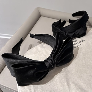 Detailed view of two black satin headbands with small rhinestones and a bow on a beige surface