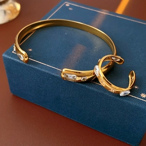 Detail of gold teardrop zircon open bangle and matching earring on blue jewelry box