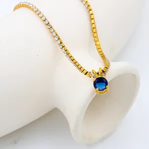 Close-up of gold tennis chain with dark blue birthstone pendant on white ceramic