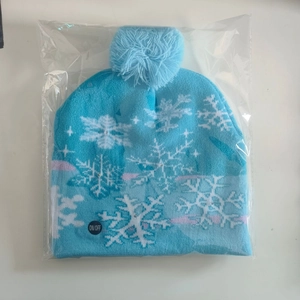Close-up of light blue knitted Christmas hat with LED power switch and snowflake pattern