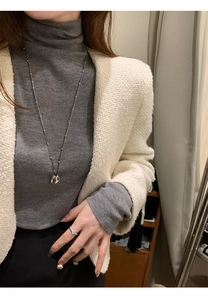 Long silver chain necklace with geometric pendant shown on a model wearing knitwear