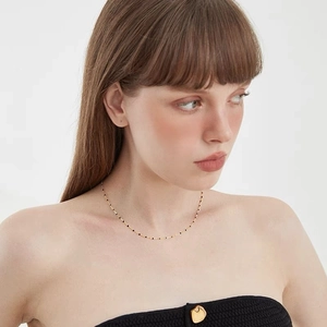 Minimalist gold chain necklace with black enamel beads worn by a model on white background