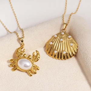 Détail de pendentifs crabe et coquillage dorés avec perles blanches sur tissu doux