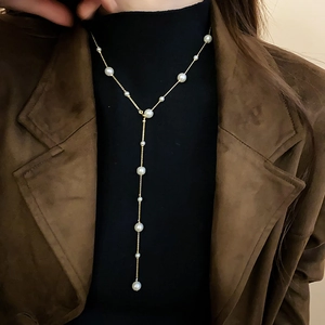 Elegant Y-shaped faux pearl necklace on a gold chain over a dark turtleneck sweater