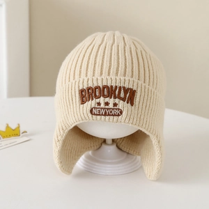 Dettaglio del ricamo Brooklyn su un cappello di maglia beige con paraorecchie per bambini