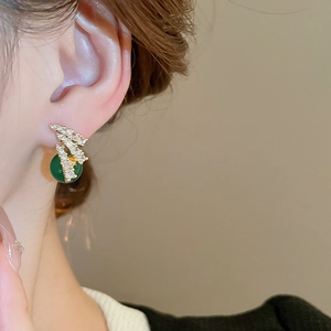 Dettaglio di orecchini dorati con perle di zircone verde indossati da una modella
