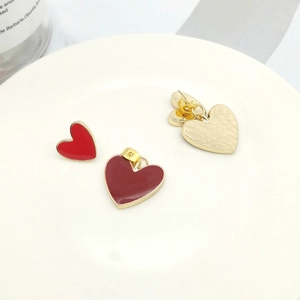 Detail of red and burgundy enamel heart earrings with gold trim on white decor