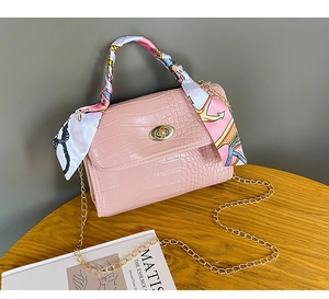 Pink stone pattern handbag with metal chain and floral silk scarf detail on wooden table