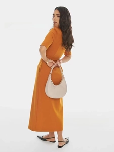 Fashionable beige half-moon handbag shown on model wearing a vibrant orange dress