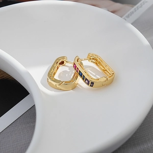 Detailed macro view of gold-plated rectangular hoops with colorful zircon stones on tray