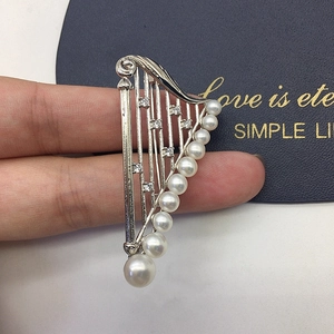 Macro detail of harp-shaped brooch featuring silver alloy frame and white pearls