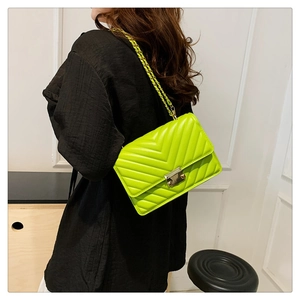 Detail of neon green chain bag with V-quilted pattern and gold buckle on a model
