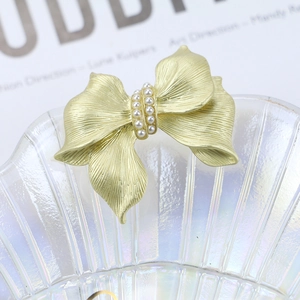 Elegant gold bow brooch with matte finish and pearls on a pearlescent glass dish