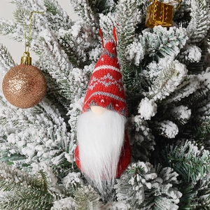 Close-up of a knitted Christmas gnome ornament with snowflake hat on a snowy tree
