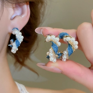 Detailed view of C-shaped blue denim and pearl twisted earrings with gold metal base